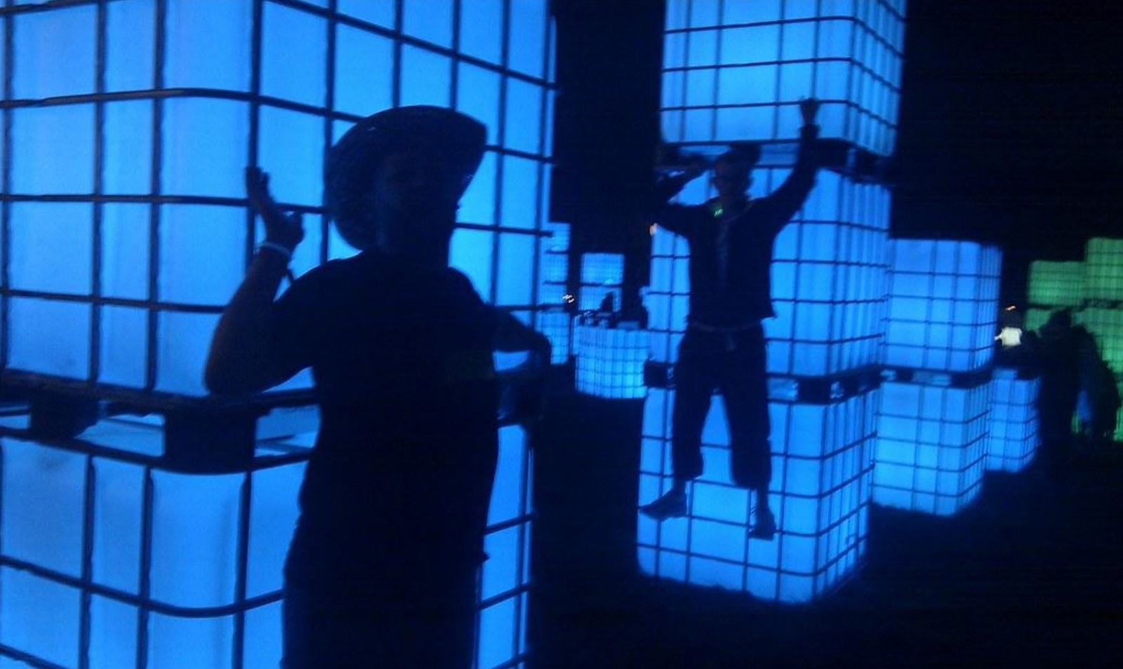 Figure 5: figures with raised hands under cool blue lighting and glowing grids.